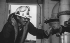 An oil worker checking equipment while wearing a modern hardhat with ear protectors. In the 1970s and 80s, new protective equipment was developed and soon made mandatory at well sites.
