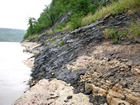 Bitumen seeping from limestone banks along the Athabasca River; in 1715, the Chipewyan woman Thanadelthur told Hudson’s Bay Company staff that a black substance oozed from the banks of a river (likely the Athabasca) in her homeland in such quantities that her people had to canoe for miles before being able to go ashore. 