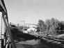 Royalite gas plant, looking west from the east side of the bridge over the Sheep River; the water pump house is in the foreground on the lower bench. The lean oil pump house is beyond it, as is the absorption plant with its five towers, ca. 1942. <br />Source: Glenbow Archives, IP-14a-768