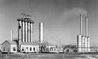 In the scrubbing plant at left, hydrogen sulfide (H<sub>2</sub>S) gas and water were removed from the gas. The actifiers at right separated the H<sub>2</sub>S from the scrubbing chemicals, and powerful fans blew the gas out the tall stacks, February 1945. <br />Source: Glenbow Archives, IP-6d-4-7b