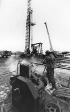 A rig worker hoses down equipment following a rig blowout, n.d. Even into the 1980s, work on the rigs involved near-constant exposure to the oil, drilling mud and other fluids and the elements (from extreme heat to extreme cold, rain, snow and biting insects). However much drilling technology had improved, some jobs just had to be done by hand and human muscle power.